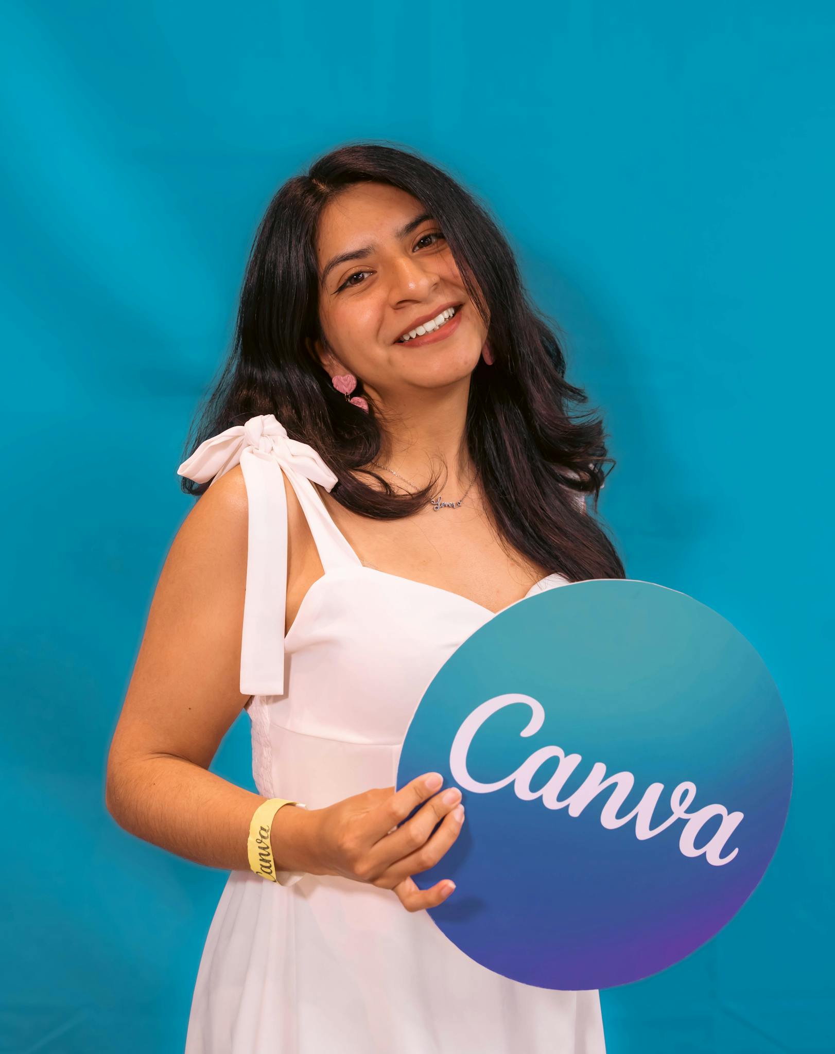 Cheerful woman in white dress holding Canva sign against vibrant blue backdrop.